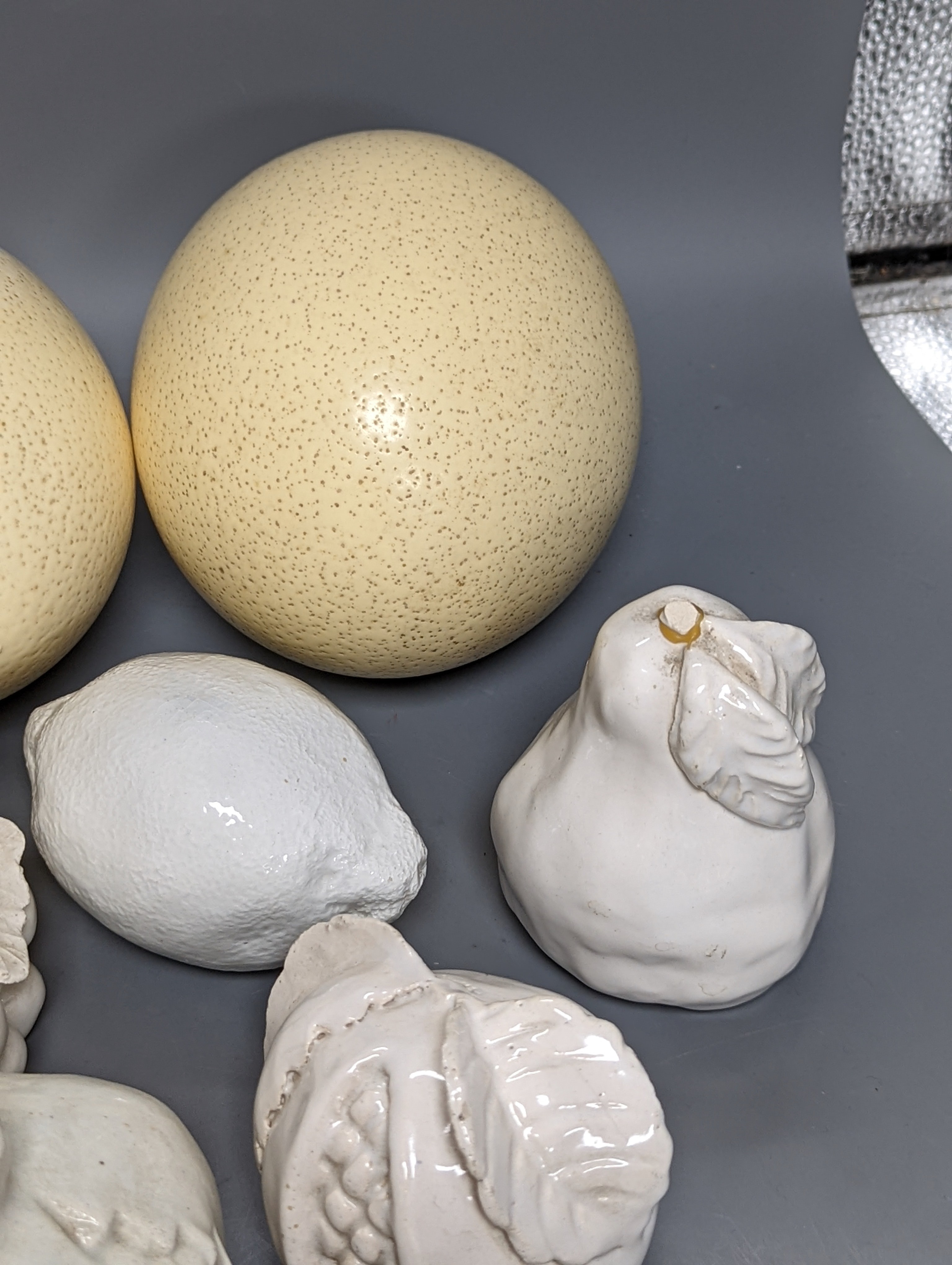 A decorative collection of tin glazed model fruits, together with three ostrich eggs